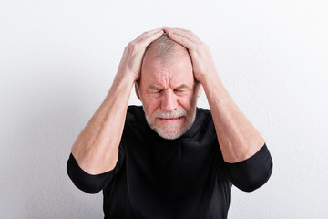 Wall Mural - Upset senior man with headache, holding his head, studio shot.