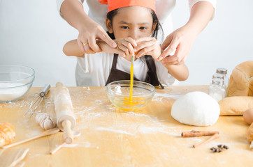 Asian little girl breaking shell of egg for making bakery