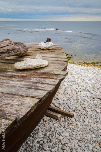 Fotografía Skiff boat on stone beach by the ocean with stones on boat cover on Gotland, Swe