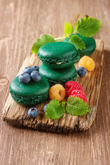 Traditional French sweets. A green makorunas with mint, white and red raspberries, blueberries on a wooden board. Dark background.