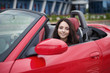 Pretty young brunette woman driving luxury red cabriolet car.