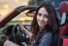 Pretty Young Brunette Woman Driving Luxury Red Cabriolet Car At The Sunset.