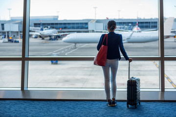 Wall Mural - Businesswoman traveling in airport. Woman looking through the window at tarmac and planes waiting for flight. Business travel concept.