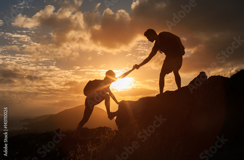 Fotografía Male and female hikers climbing up mountain cliff and one of them giving helping hand