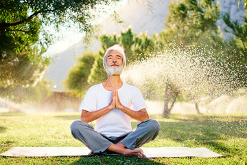 Wall Mural - Yoga at park. Senior bearded man in lotus pose sitting on green grass. Concept of pray and meditation.