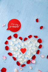 Heart of red, white rose petals on blue painted rustic background. Valentines day or love concept. Fresh natural flowers. I love you so much.