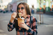© Oleksandr Kozak - Beautiful smiling young female in sun glasses eating fast food on cities background