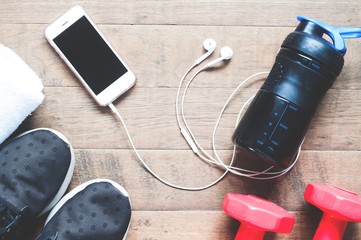 Wall Mural - Flat lay of mobile phone with earphones and sport equipments on wood background. Workout and fitness items, top view