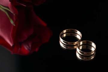 close-up of two gold wedding rings and wedding bouquet of red roses on black background. gold rings 