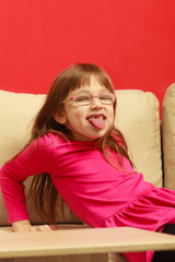 Wall Mural - Toddler girl sitting on sofa sticking tongue out