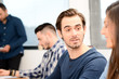 © W PRODUCTION - portrait of a candid handsome young man in high school classroom talking with woman friend classmate with teacher in background