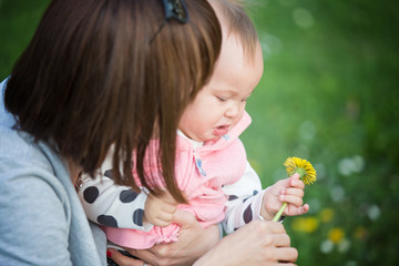 Wall Mural - Mother holding her one year old sad baby girl, who has a dandelion in her hand; baby's face is sad and showing discomfort