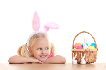 Wall Mural - Cute little girl with bunny ears and basket full of Easter eggs on white background