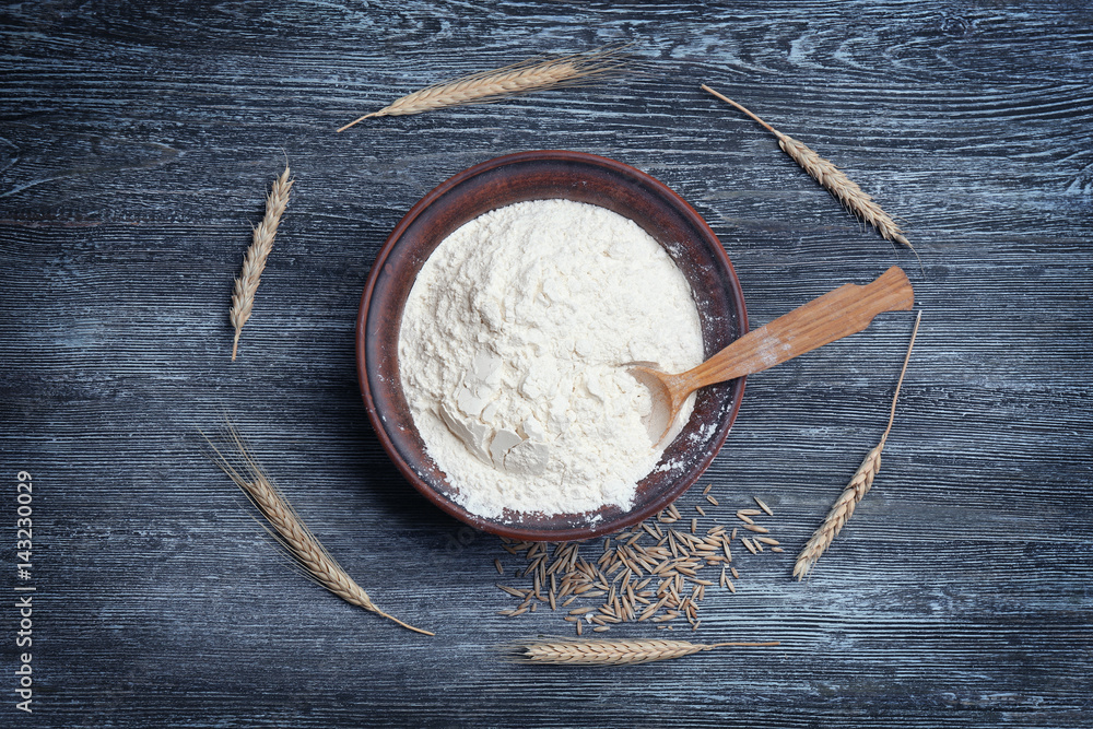 Bowl with flour, spoon and wheat on wooden table