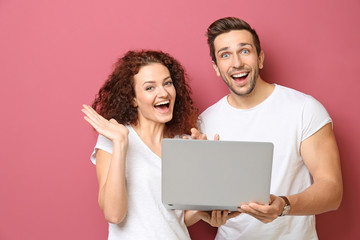 Happy young couple with laptop on color background