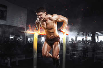 Wall Mural - Muscular bodybuilder working out in gym doing exercises on burning fire parallel bars. Concept sport