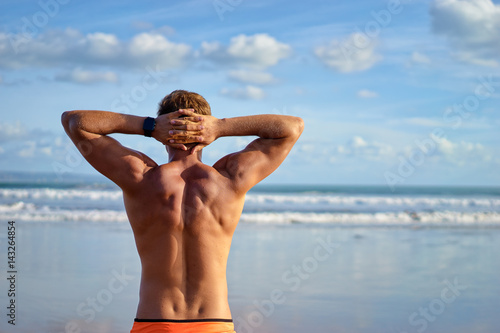 Plakat Wakacje na plaży. Tylny widok zrelaksowany młody mięśniowy mężczyzna cieszy się dennego widok.