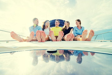 Wall Mural - Friendship and vacation. Group of laughing young people sitting on the yacht deck sailing the sea.