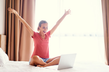 Happy winner! Good news. Excited young woman working on laptop computer at her bedroom.