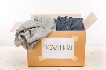Wall Mural - cardboard box with donation clothes on wooden table on white, donation concept