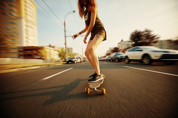 Beautiful young girl with tattoos riding longboard in sunny weather