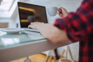 Close up and part of human hand using laptop and holding coffee cup