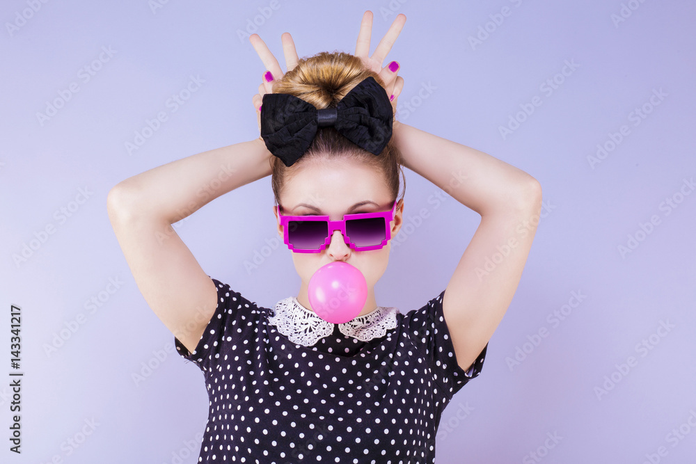 Portrait humoristique d'une jeune femme faisant une bulle de chewing gum les doigts en "V" derrière la tête