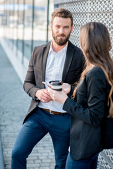 Caucasian business couple talking together standing outdoors during the coffee break near the modern building facade