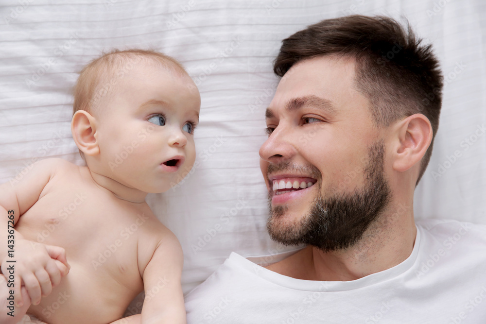 Father lying with cute baby daughter on bed at home
