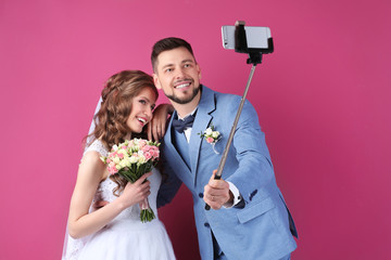 Wall Mural - Happy wedding couple making selfie on color background