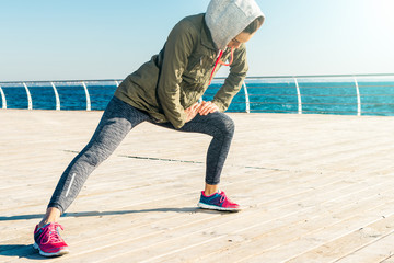 Wall Mural - Woman in jacket, hoodie and sneakers doing sports exercises on the beach