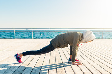 Wall Mural - Woman in jacket and hood doing stretching on beach in the morning