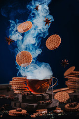 Wall Mural - Steaming cup of tea with flying cookies and spices