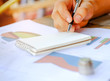 © sarawutnirothon - Concept business,Pen in hand on notebooks with coins placed on graph.
