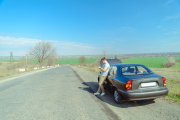 Wall Mural - Angry young man waiting a help while sitting near the broken car