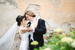 © andriychuk - Groom in black tailcoat hugs bride tender before ruined wall