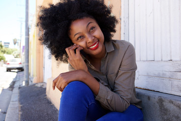 Wall Mural - attractive african woman sitting on steps with mobile phone