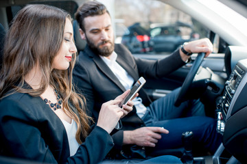 Businesswoman showing phone to the businessman sitting together on the front in the car