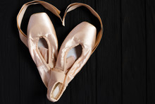 Ballet Pointe Shoes On Black Wooden Background With Ribbons In Shape Of A Heart