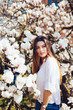 © F8  \ Suport Ukraine - Outdoor portrait of a young beautiful woman near magnolia tree with flowers. Girl wearing stylish clothes. Female spring mood