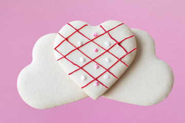 horizontal image of two white heart shaped cookies with one decorated heart shape cookie lying on top on light pink background