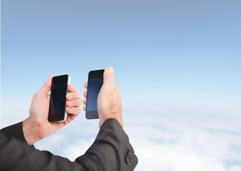 Canvas Print - Hands holding two phones at same time against blue sky