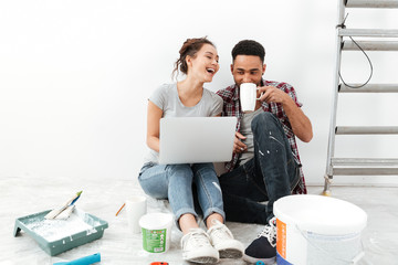 Wall Mural - Laughing young loving couple sitting on floor in new flat