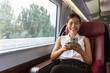 © Maridav - Smiling Asian businesswoman using smartphone social media app while commuting to work in train. Woman sitting in transport enjoying travel.