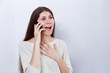 © mark_ka - Portrait of a happy young woman talking on the phone and having received good news. Human reaction, expression. Grey background.