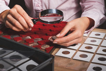 Box With Collectible Coins In The Cells And A Hand With Coin Through The Magnifying Glass