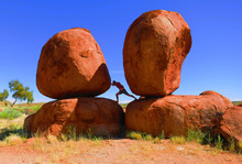 Bearded Man Attempting To Push Over A Huge Boulder Rock In The The 'Devils Marbles' - An Interesting Natural Rock Formation In The Outback Of Australia, Northern Territory