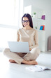 © deagreez - Vertical portrait of young pretty woman in glasses sitting on the floor at home and using laptop