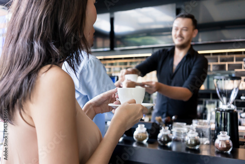 Fotomural Young woman holding a white cup of coffee next to her partner in a modern coffee