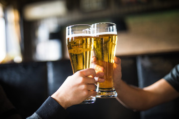 cheers. close-up of two men in shirts toasting with beer at the bar counter